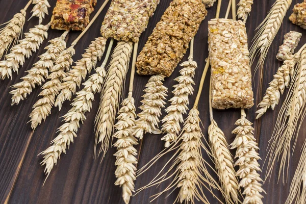 Cereal energy granola bars and spikelets of wheat on dark wooden background. Natural source of energy. Top view. Close up