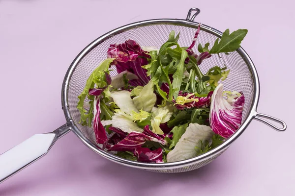 Multicolored vegetable mix in metal colander. Vegan food. Clean eating. Pink background