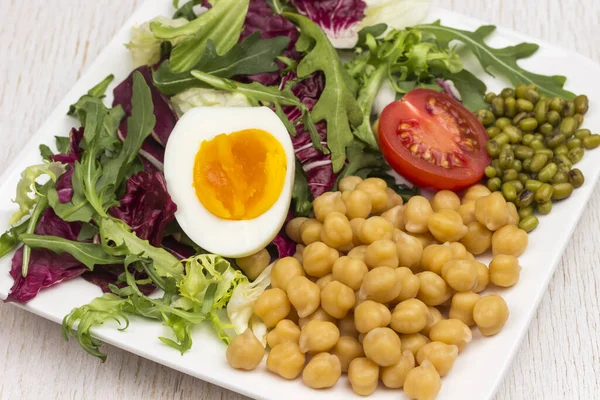 Multicolored vegetable mix, chickpeas, mung bean, egg and tomato in black plate. Balanced nutrition. White background