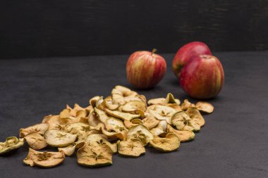 Üç taze kırmızı elma ve siyah arka planda kurutulmuş elma dilimleri. Vejetaryen yemeği. Boşluğu kopyala