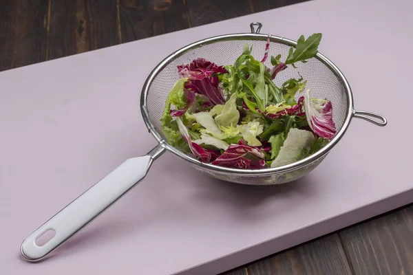 Multicolored leafy vegetable mix in metal colander. Vegan food. Clean eating. Pink background