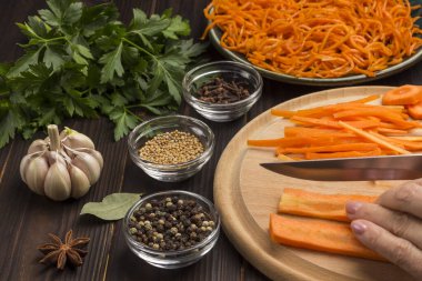 Eller kesme tahtasında çiğ havuç doğruyor. Baharat, sarımsak ve maydanoz. Tabakta mayalanmış havuç. Bağışıklığı güçlendirmenin doğal kaynağı. Yakın plan. Koyu tahta arkaplan