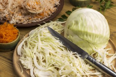 Dilimlenmiş çiğ lahana, kesme tahtasında bıçak. Havuç ve tuzlu lahana tabakta. Ev yapımı Fermantasyon Ürünleri. Kapat.