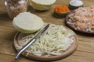 Dilimlenmiş çiğ lahana, kesme tahtasında bıçak. Havuç ve tuzlu lahana tabakta. Ev yapımı Fermantasyon Ürünleri. Kapat.