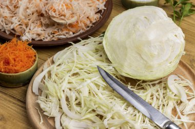 Havuç ve tuzlu lahana tabakta. Dilimlenmiş çiğ lahana, kesme tahtasında bıçak. Ev yapımı Fermantasyon Ürünleri. Kapat.