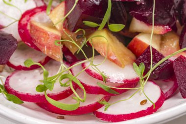 Dilimlenmiş haşlanmış pancar, dilimlenmiş turp ve taze mikroyeşil lahanalı elmalardan oluşan besleyici bir salata. Kapat.