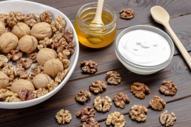 Ceviz çekirdekleri ve beyaz seramik kasede ceviz, masada ballı ve yoğurtlu cam kavanoz. Koyu ahşap arka plan. Üst görünüm