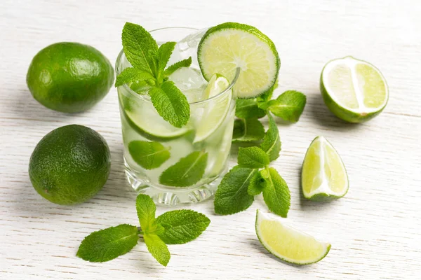 Summer cooling drink with ice, lime and mint. Non-alcoholic beverage. White wooden background.