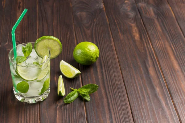 Summer cooling drink with ice, lime and mint. Non-alcoholic beverage. Dark wooden background. Copy space