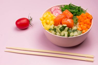 Geleneksel Hawaii kırmızı balık kasesi pirinç, turp, salatalık, domates ve yosunlu. Buda kasesi. Diyet yemek. Pembe arka planda bambu yemek çubukları