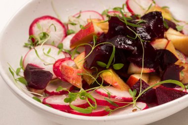 Dilimlenmiş haşlanmış pancar, dilimlenmiş turp ve taze mikroyeşil lahanalı elmalardan oluşan besleyici bir salata. Kapat.