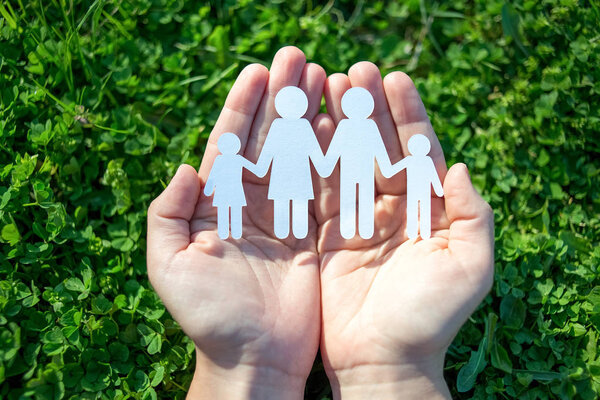 Paper family in two hands on green grass background