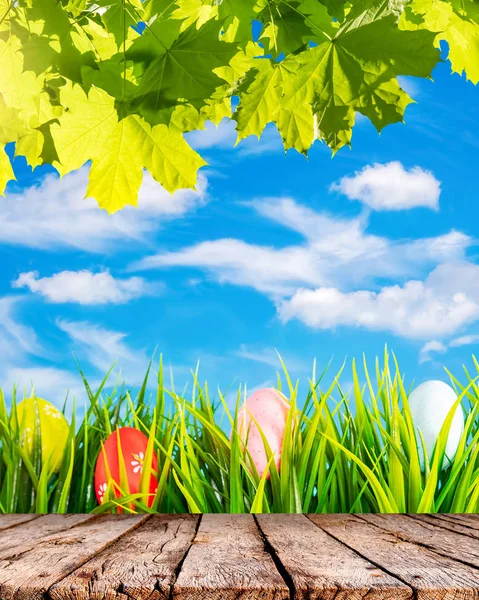 Osterhintergrund mit bunten Eiern im grünen Gras, blauem Himmel und weißen Wolken — Stockfoto