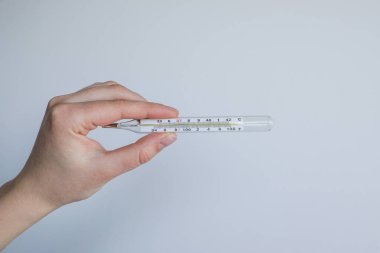 Vücut ısısını gösteren termometreyi tutan bir el.