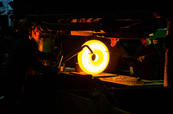 workers hold the workpiece under the hammer