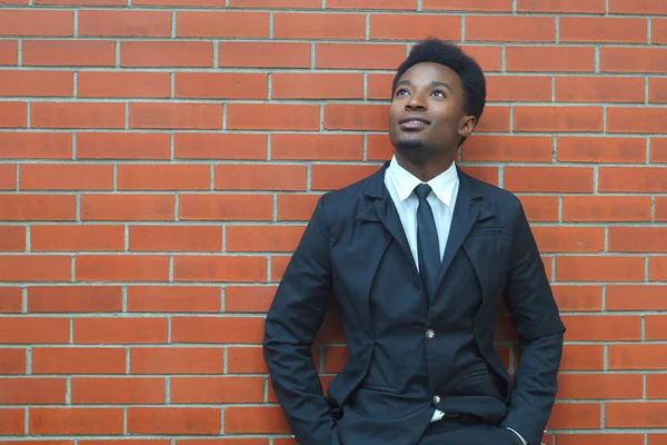 Fiatal üzletember álló keresi fel öltöny és a nyakkendő, kezelő téglafal háttér — Stock Fotó