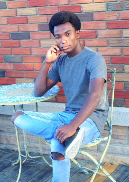 Jonge Afrikaanse man denken buiten stoep stad tabel jeans t-shirt ontspannen man — Stockfoto
