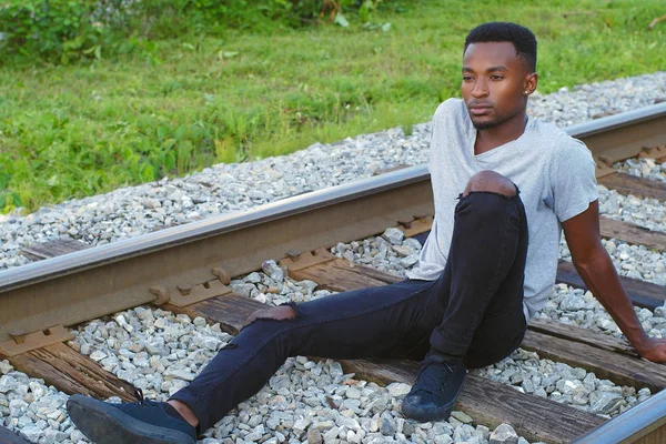 Fiatal afrikai férfi ül a vonat pályán magány életmód — Stock Fotó