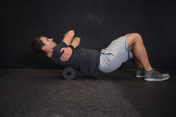 Spor salonunda yerde bir köpük rulo kullanan adam