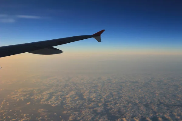 Wing of an airplane flying above the clouds at sunset — Stock Photo, Image