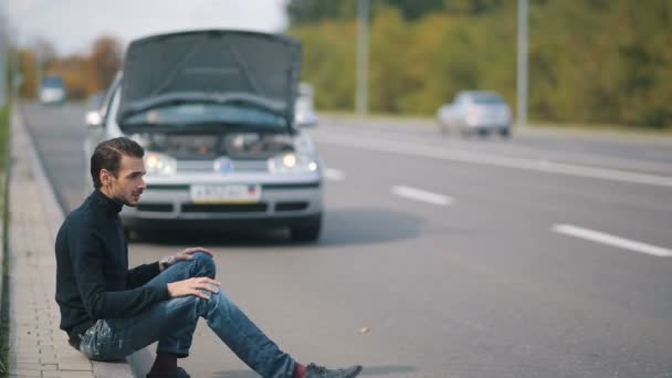 Man zit in een front van kapotte auto op de weg — Stockvideo