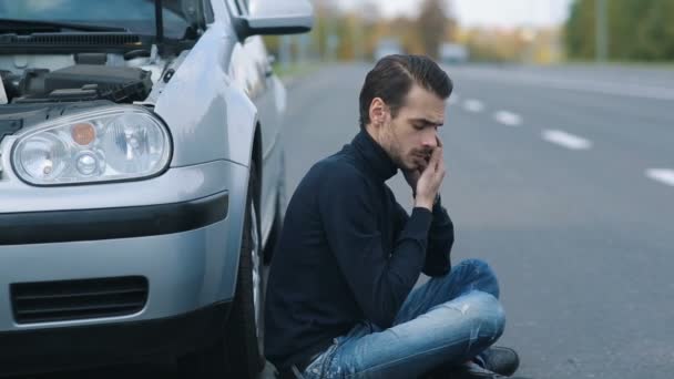 Człowiek siitting w pobliżu uszkodzonego samochodu i wezwał do pomocy — Wideo stockowe