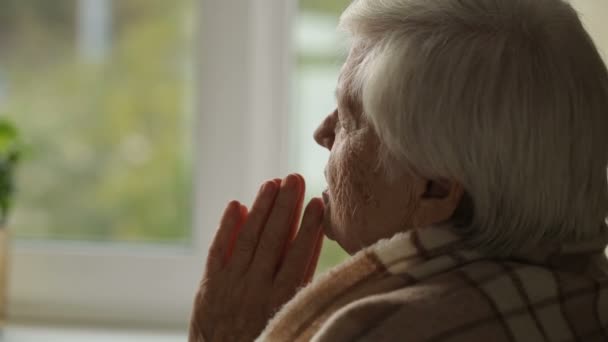 Anciana rezando en una fron de ventana — Vídeo de stock