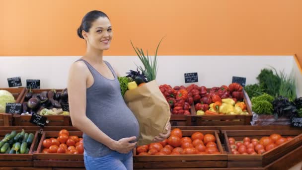 Gravid kvinna med påse med grönsaker i butik — Stockvideo