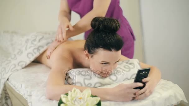 Massör gör massage till kvinna med smartphone — Stockvideo