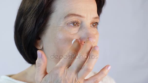 Mujer de mediana edad aplicando crema en la cara — Vídeos de Stock