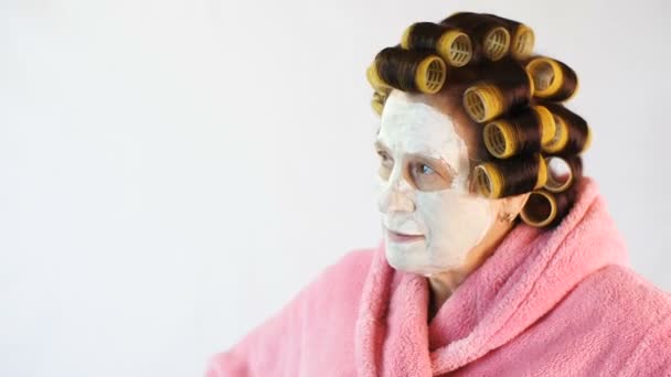 Boze vrouw met een cosmetische masker en krulspelden — Stockvideo