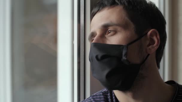 Droevige man met beschermend masker kijk naar het raam — Stockvideo