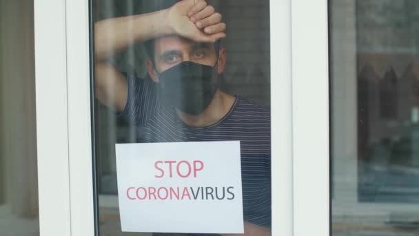 Hombre con una máscara protectora con la inscripción "Stop coronavirus" fuera de la ventana — Vídeo de stock