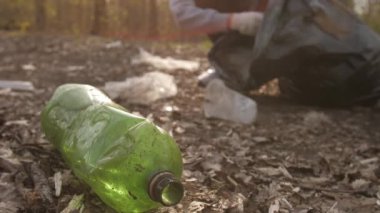 Kadın yerden eski plastik şişeleri topluyor.