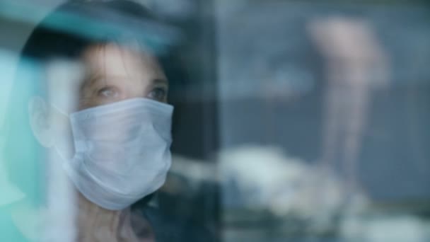 Mujer madura en máscara de protección médica mira por la ventana — Vídeos de Stock