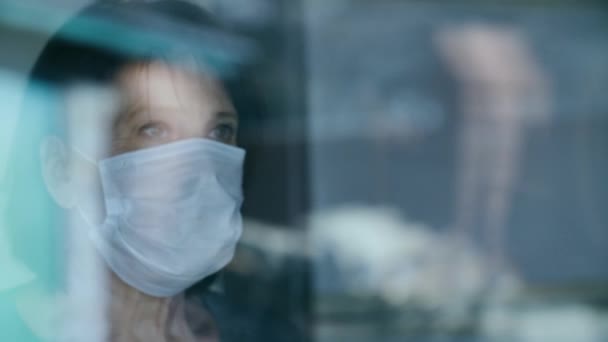 Reife Frau in medizinischer Schutzmaske schaut aus dem Fenster — Stockvideo