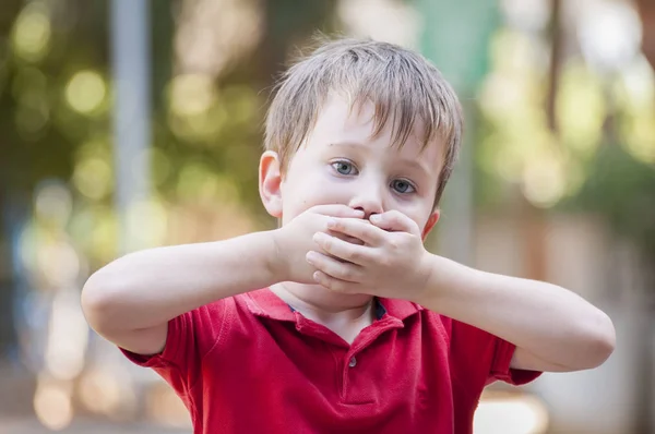 Poważne mały chłopiec kaukaski zamknięcia jego usta rękami. — Zdjęcie stockowe
