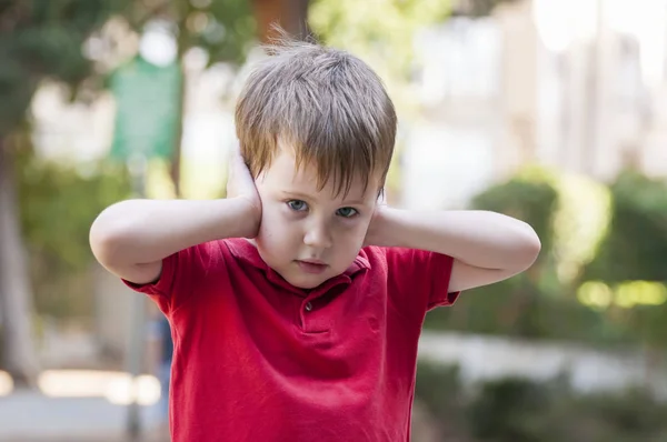 Koppig Kaukasische jongetje sluiten oren met zijn handen en kijken naar de camera. — Stockfoto