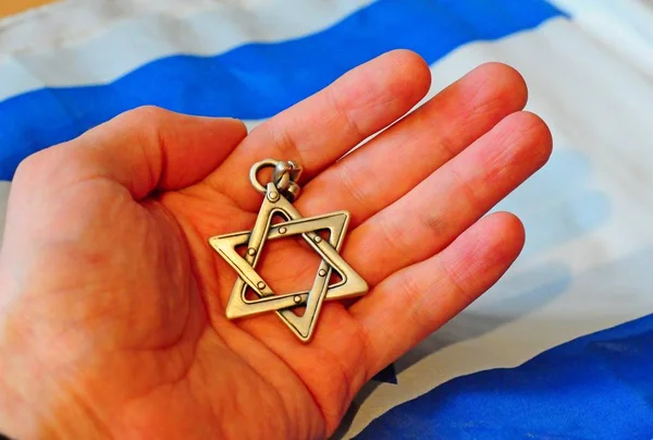Hand holding a Jewish Star of David with Israel flag on the background. — Stock Photo, Image