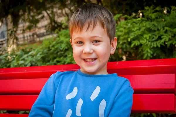 Feliz niño caucásico sonriente sentado en el banco . —  Fotos de Stock