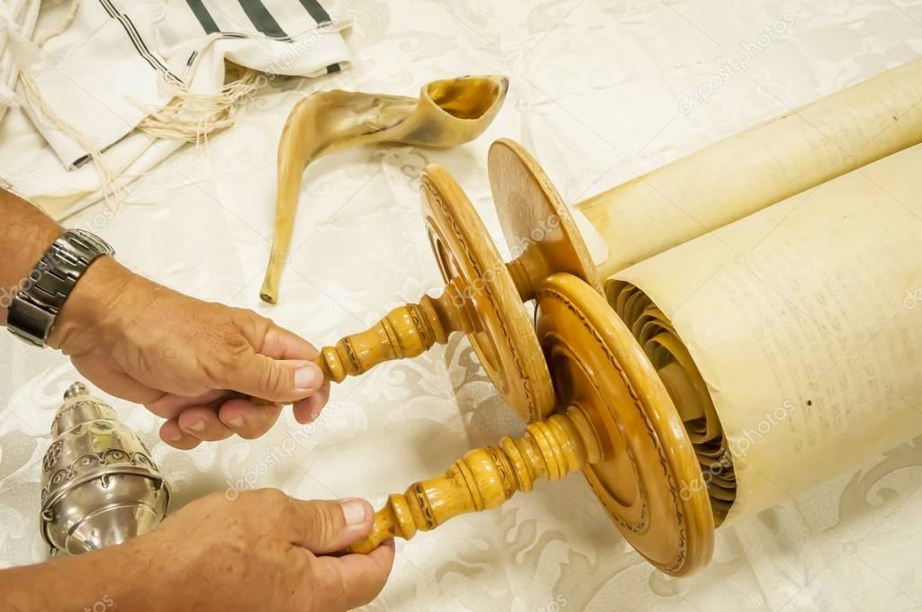 Hands of a Caucasian man holding the handles of the Torah scrolls.