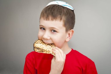 Beyaz kippah şapkalı beyaz beyaz beyaz çocuk shmura matzo yiyor. Pessakh için mayasız bir parça geleneksel Yahudi ekmeği. Yahudi bayramı..