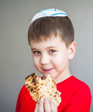 Beyaz kippah şapkalı beyaz beyaz beyaz çocuk shmura matzo yiyor. Pessakh için mayasız bir parça geleneksel Yahudi ekmeği. Yahudi bayramı..