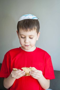 Beyaz kippah şapkalı beyaz beyaz beyaz çocuk shmura matzo yiyor. Pessakh için mayasız bir parça geleneksel Yahudi ekmeği. Yahudi bayramı..