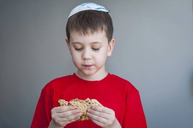 Beyaz kippah şapkalı beyaz beyaz beyaz çocuk shmura matzo yiyor. Pessakh için mayasız bir parça geleneksel Yahudi ekmeği. Yahudi bayramı..