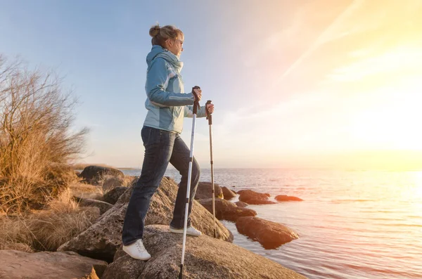 Happy girl with Hiking sticks at a lake on the rocks. Estonia