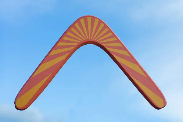 Hölzerner australischer Bumerang im Flug vor rein weißen Wolken und blauem Himmel — Stockfoto