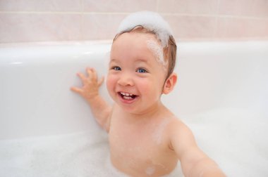 Kafasında köpük olan küçük bir kız banyoda gülümsüyor. Sevimli kız bebek banyoda mutlu. Sevimli küçük bebek portresi. Cilt bakımı. Sağlık hizmetleri. Mutlu aile.