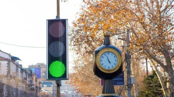 Time lapse: semáforos con un reloj en el fondo de la ciudad con árboles . — Vídeos de Stock