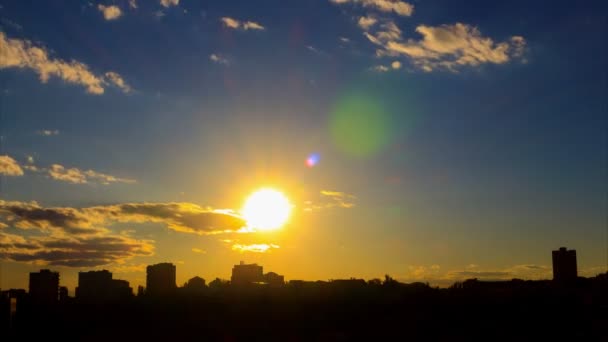 회색-흰색 구름, 푸른 하늘, 렌즈 플레어, 도시 실루엣의 배경으로 황금 태양, 일몰의 아름 다운 시간 경과. 아름다움 — 비디오